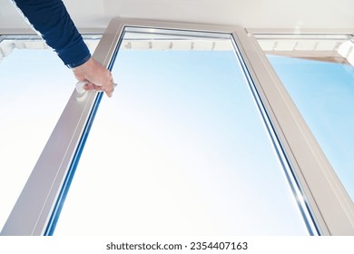 A man hand opens window frame. Room glazing. Window frame installing and service. One sided open window. Apartment ventilation through window. View from the bottom