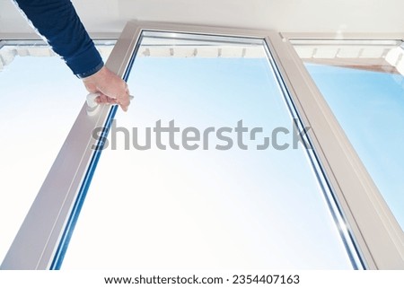 A man hand opens window frame. Room glazing. Window frame installing and service. One sided open window. Apartment ventilation through window. View from the bottom
