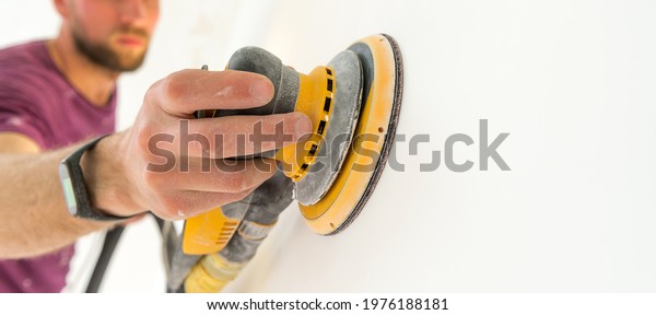 Man hand polishing surface after putty for\
painting. Using hand polishing machine for cement wall.Home\
improvement worker in protective mask and glasses working with\
sander for smoothing wall\
surface.