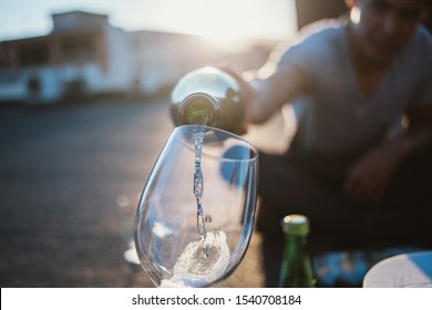 Man Hand Pouring White Wine From The Bottle Into Glasses With Friends Outside