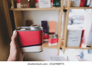 A man hand prepares to brew by holding coffee beans wrapped in an aluminum can, with a bokeh background of a display case from a coffee shop or restaurant - Powered by Shutterstock