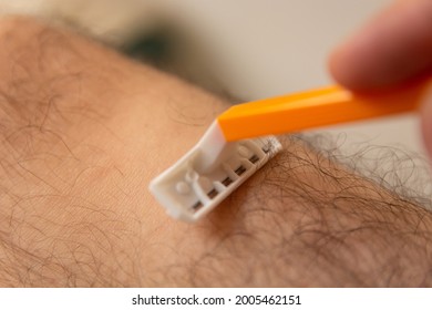 A Man Hand With Razor Shaving Hairy Legs At Home. Man Beauty Concept. Close Up, Selective Focus And Copy Space