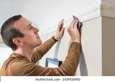 Man hand sands nail filling to install white wood trim crown moulding - Powered by Shutterstock