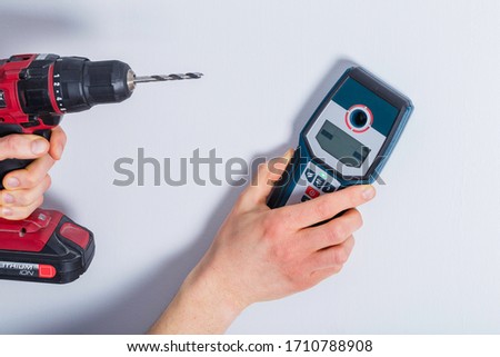 Man hand is scanning wall by cable detector to find a cable before drilling in.