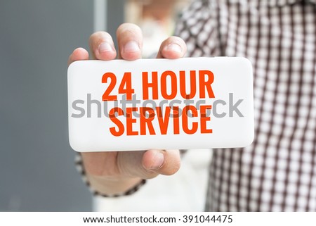 Man hand showing 24 HOUR SERVICE word phone with  blur business man wearing plaid shirt.