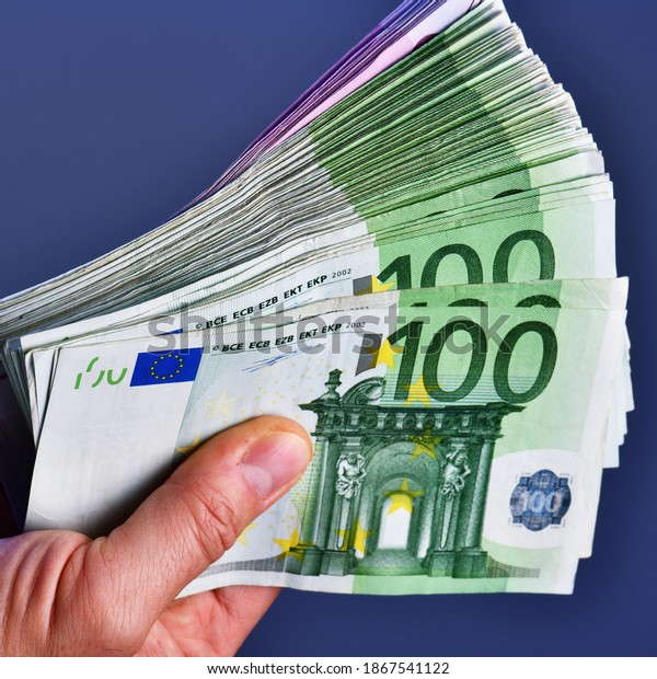 A man hand shows 20,000 Euros in 100\
euro and 500 euro banknotes on a blue\
background.
