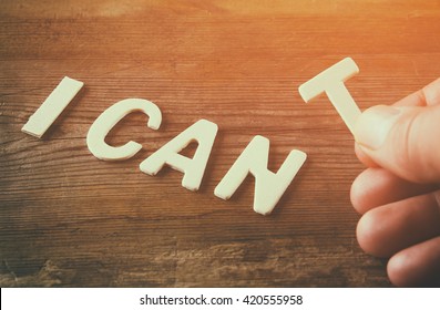 man hand spelling the word I CAN'T from wooden letters, cutting the letter T so it written I CAN. success and challenge concept. retro style image
