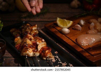 Man Hand Sprinkling Salt And Seasoning On Grilled Skewers Of Chicken And Vegetables