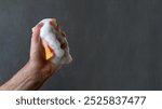 Man hand  squeezes washing sponge with white soapy foam isolated on gray background