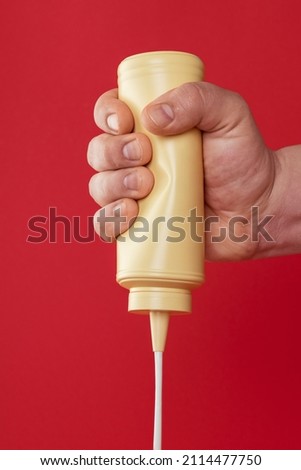 Man hand squeezing a bottle of mayo against a red-colored background. Pouring mayonnaise from a plastic bottle.