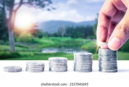 Man hand stacked coins with money saving concept and profit graph business finance in a piggy bank with money boxes for future funds of tourism, home, and retirement on a blurred background. - Shutterstock ID 2157045693