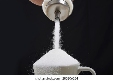 Man Hand With Sugar Bowl Pouring A Crazy Lot Of It Spilling Out Everywhere In Full Coffee Cup In Insane Sugar Addiction And Unhealthy Nutrition Concept Isolated On Black Background