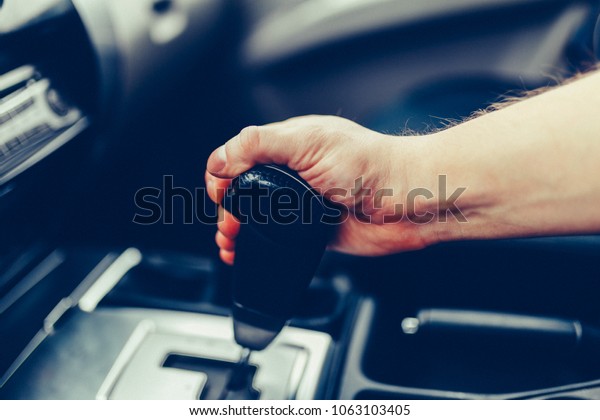 The man hand switches the automatic transmission\'s\
close-up. Close-up of the driver\'s arm includes mode Drive on the\
gear lever automatic transmission of the car interior parts.\
Stylish Toned Photo