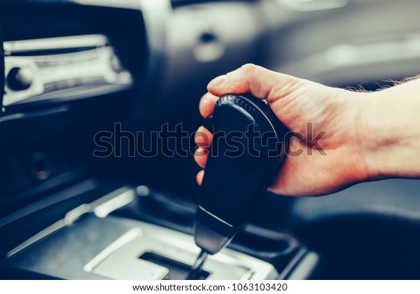 The man hand switches the automatic transmission\'s\
close-up. Close-up of the driver\'s arm includes mode Drive on the\
gear lever automatic transmission of the car interior parts.\
Stylish Toned Photo