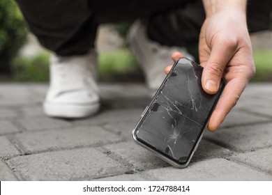 Man hand take broken damaged smartphone from asphalt
