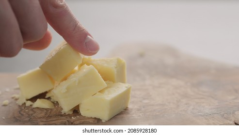 Man Hand Takes Cheddar Cheese Cube From Olive Wood Board Closeup