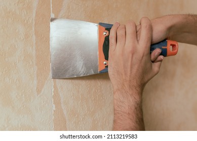 Man Hand Tearing Off Old Wallpaper With Scraper From Wall.