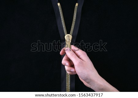 Man hand unzips a gold zipper on maroon background                