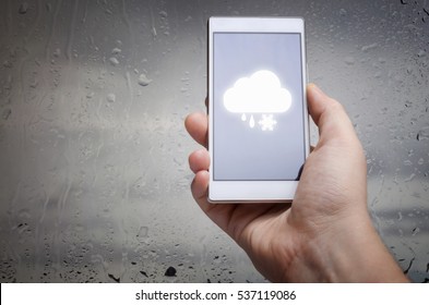 Man hand using mobile smart phone with glass window full of water droplets of raining day view with weather forecast widget mobile application program template - Shutterstock ID 537119086
