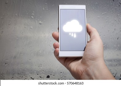 Man hand using mobile smart phone with glass window full of water droplets of raining day view with weather forecast widget mobile application program template