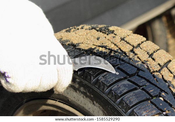 A man hand in a white work glove remove\
a nail from punctured car tire with a\
knife