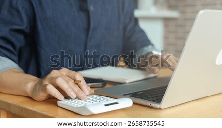man hand write on notebook and calculate on calculator about debt bills pay monthly at the table in office and manage expense payroll for money risk and crisis financial and work from home concept