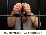 A man in handcuffs in a cell behind bars. Concept: a prisoner in a courtroom, a court sentence to a convicted person, a prison term.