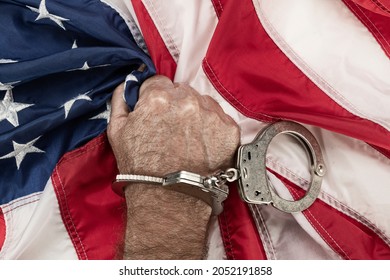 A man in handcuffs grasps the American flag in frustration and anger as oppression and bureaucracy prevent his freedom.