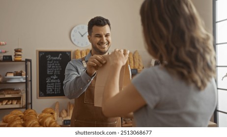 Man handing bag to woman in bakery interior with pastries and bread in background while smiling during transaction - Powered by Shutterstock