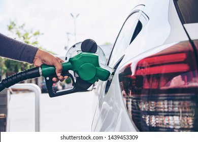 Man Handle pumping gasoline fuel nozzle to refuel. Vehicle fueling facility at petrol station. White car at gas station being filled with fuel. Transportation and ownership concept.