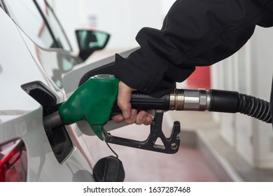 Man Handle pumping gasoline fuel nozzle to refuel. Vehicle fueling facility at petrol station. White car at gas station being filled with fuel. Transportation concept.