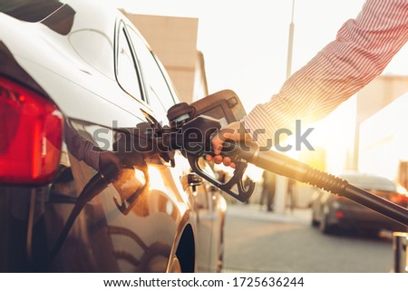 Man handle pumping gasoline fuel nozzle to refuel at petrol station. Transportation and ownership concept. Sunset lighting
