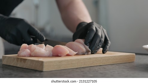 Man Hands In Black Gloves Cutting Chicken Fillet On Oak Board