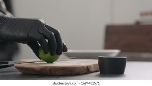man hands in black gloves take lime on olive wood board