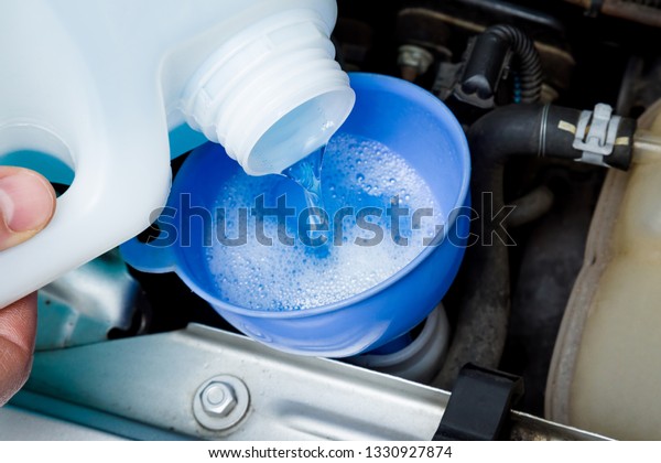 Man hands filling blue washer fluid in\
car tank through funnel from plastic bottle for windshield in\
garage. Care about automobile. Closeup. Top\
view.