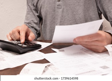 Man hands, a finger on button of calculator with financial documents in a hand and others on the table