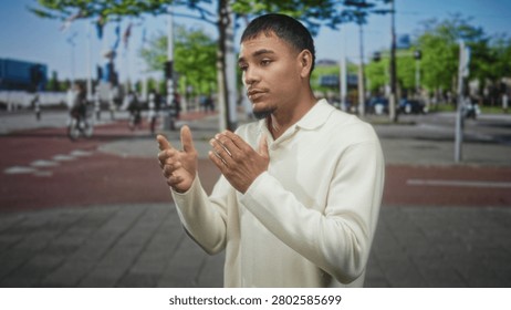 Man with hands gesturing and speaking on a busy street near flags and bicycles, wearing cream sweater; thoughtful reflection.