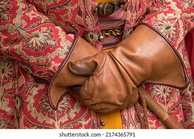 Man Hands Are Gloved And An Ornate Vintage Robe With Retro Weapons Behind An Old Belt. Male Hands In Antique Clothes With A Cane