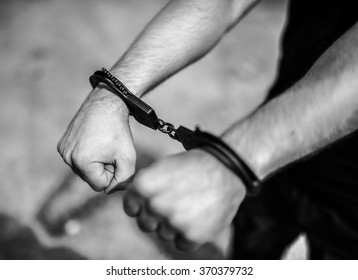 A man hands in handcuffs. Selective focus with shallow depth of field. Black and white toning.