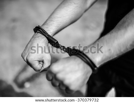 A man hands in handcuffs. Selective focus with shallow depth of field. Black and white toning.