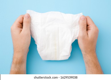 Man Hands Holding New White Baby Diaper On Pastel Blue Table Background. Point Of View Shot. Closeup.