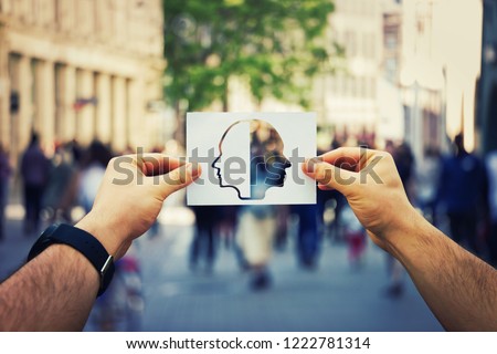 Man hands holding a white paper sheet with two faced head over a crowded street background. Split personality, bipolar mental health disorder concept. Schizophrenia psychiatric disease.