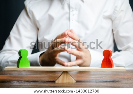 A man with hands in the lock and looks at the rival red and green figures on a scales. The concept of conflict resolution and the search for a compromise in the dispute. Weighted decision