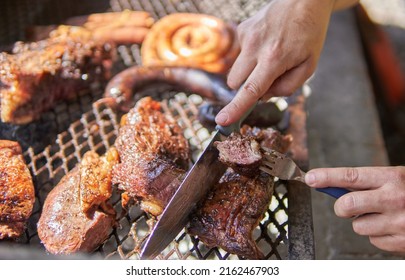 Man Hands Making Barbecue For The Lunch. Meat Cuts, Coils Of Barbecued Sausage And A Blood Sausage, Beef On An Iron Grill. Traditional Argentinian Bbq. Asado Argentino