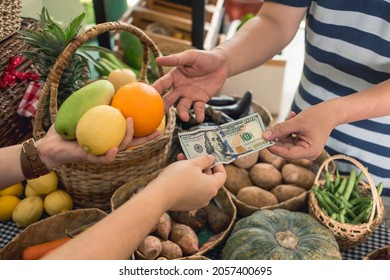 A Man Hands Over A 100 Dollar Bill To A Vendor Pay For A Few Fruits. A Purchase At A Small Market Stall.