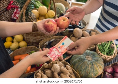 A man hands over a 50 peso bill to pay for two apples. Buying fruits at a small market stall.