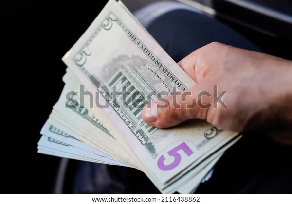 A man hands over money in a car. A wad of dollars\
in his hand.