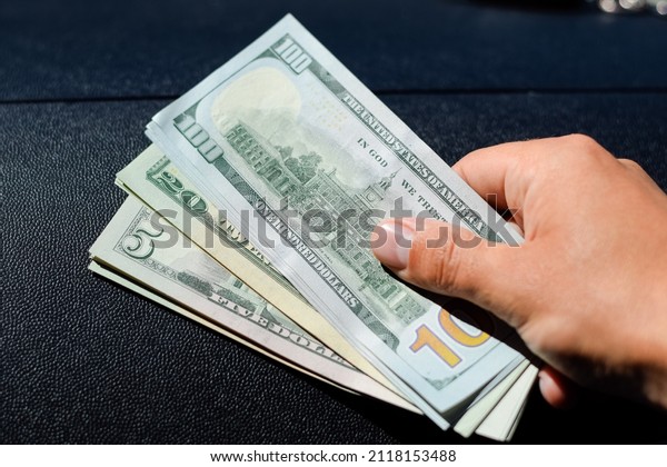 A man hands over money in a car. A wad of dollars\
in his hand.