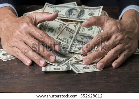 Man hands in pinstripe suit sweeping pile of us banknotes on old wooden table,business concept.Pile of money.