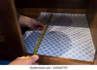 Man hands placing protective adhesive liner sheet, yellow measuring tape inside on wooden cabinets in kitchen drawers - Powered by Shutterstock